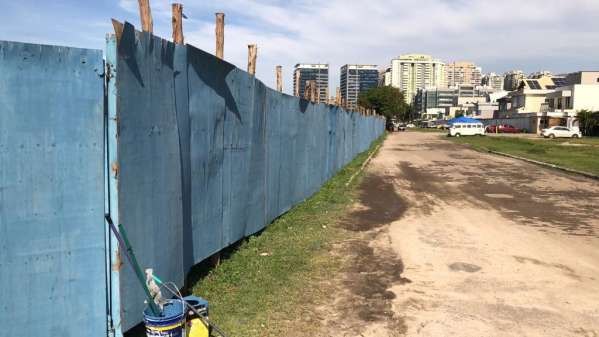 Antes: terreno cercado por tapume azul, com calçada de terra